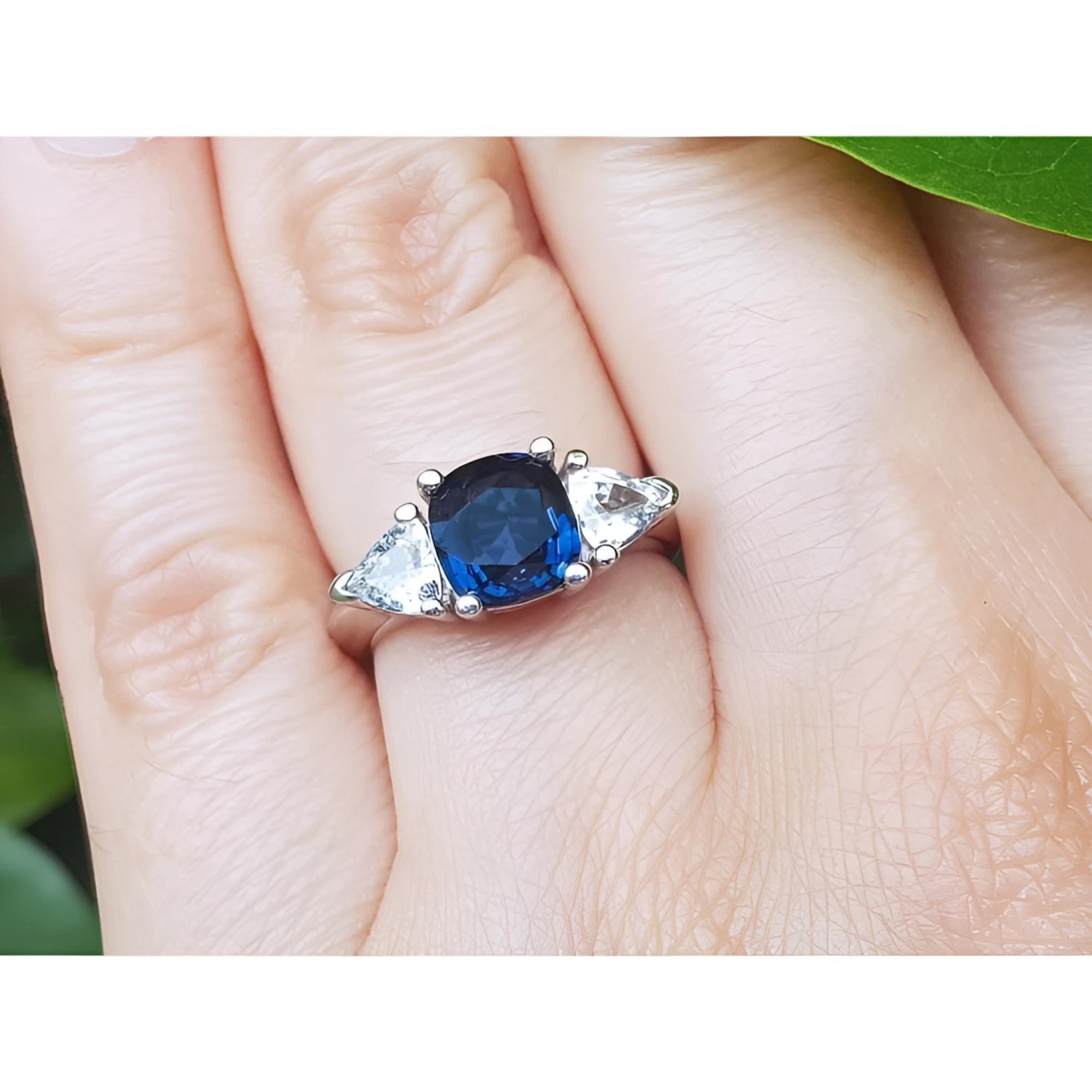 Deep blue cushion cut sapphire ring with trillion side sapphires in white gold.