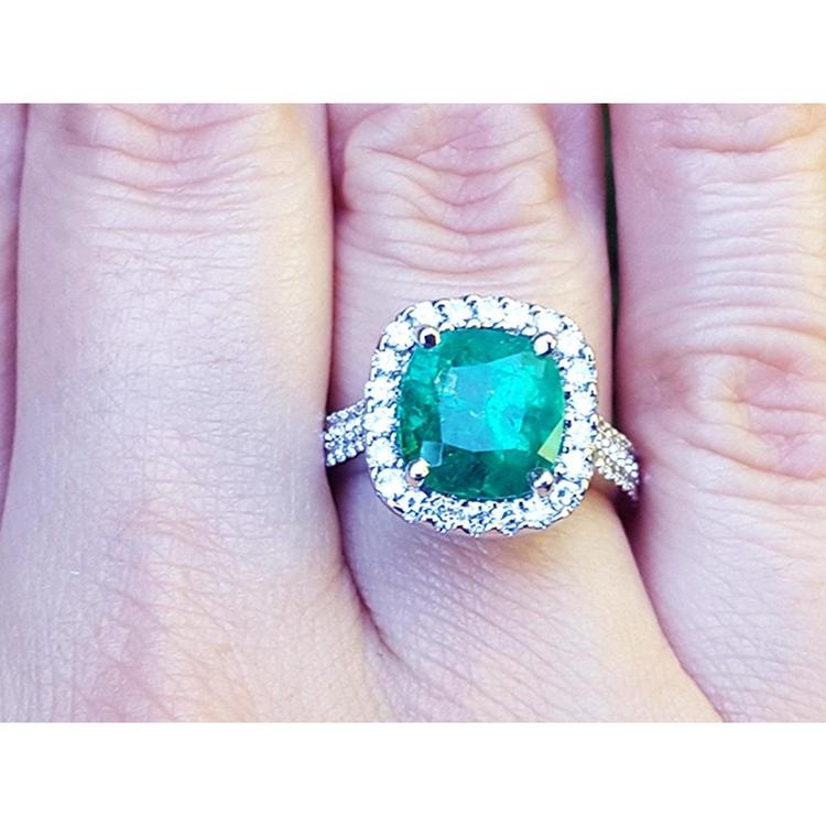Cushion cut 3.92 ct. natural emerald ring with diamond halo in 14K white gold, worn on a finger.