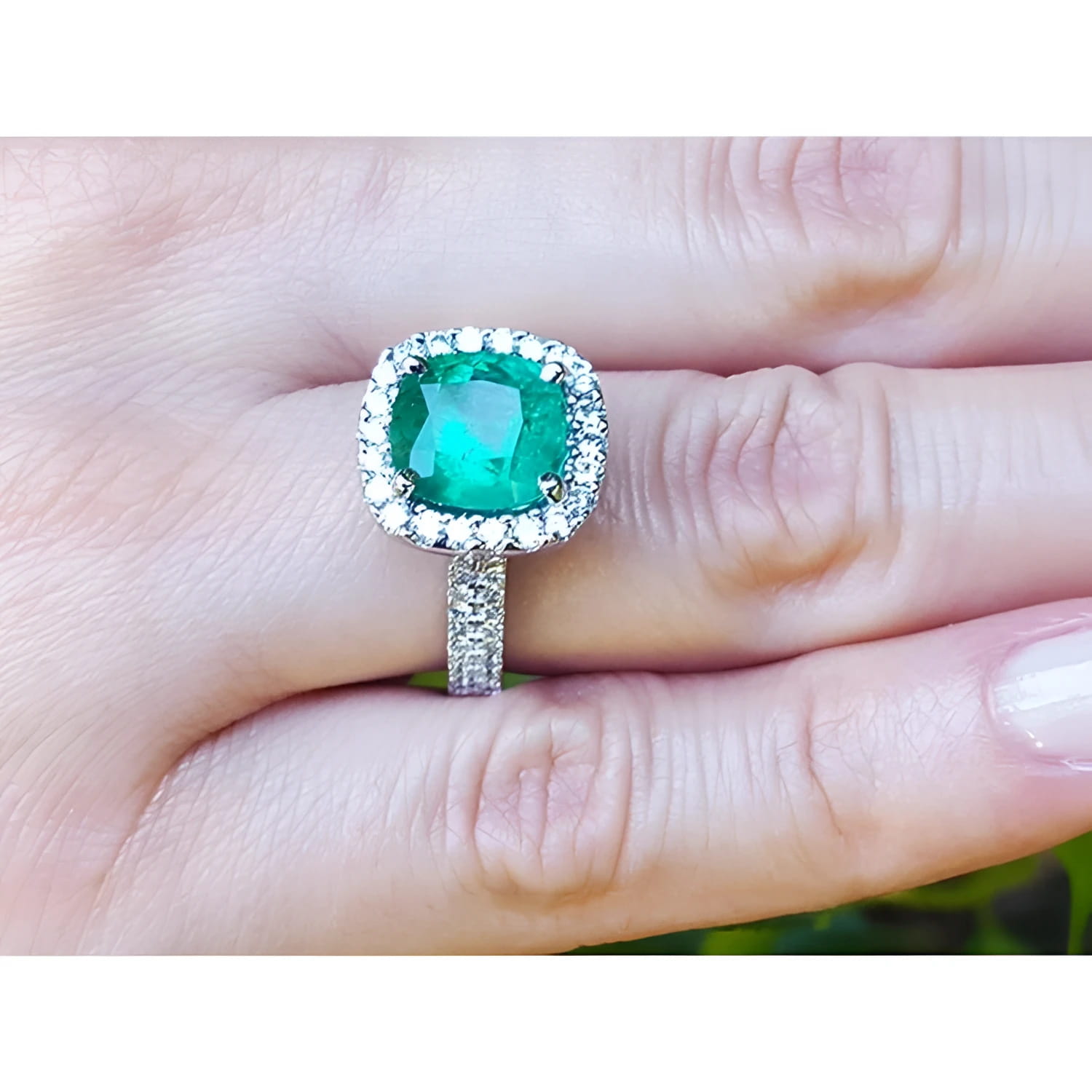 Cushion cut 3.92 ct natural emerald ring with diamond halo and band in 14K white gold on a hand.