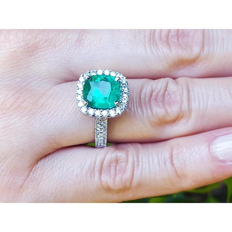 Cushion cut 3.92 ct natural emerald ring with diamond halo and band in 14K white gold on a hand.