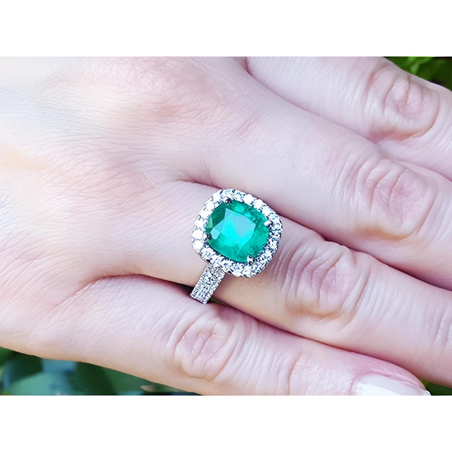 Cushion cut 3.92 ct natural emerald ring with diamond halo and band in 14K white gold on a hand.