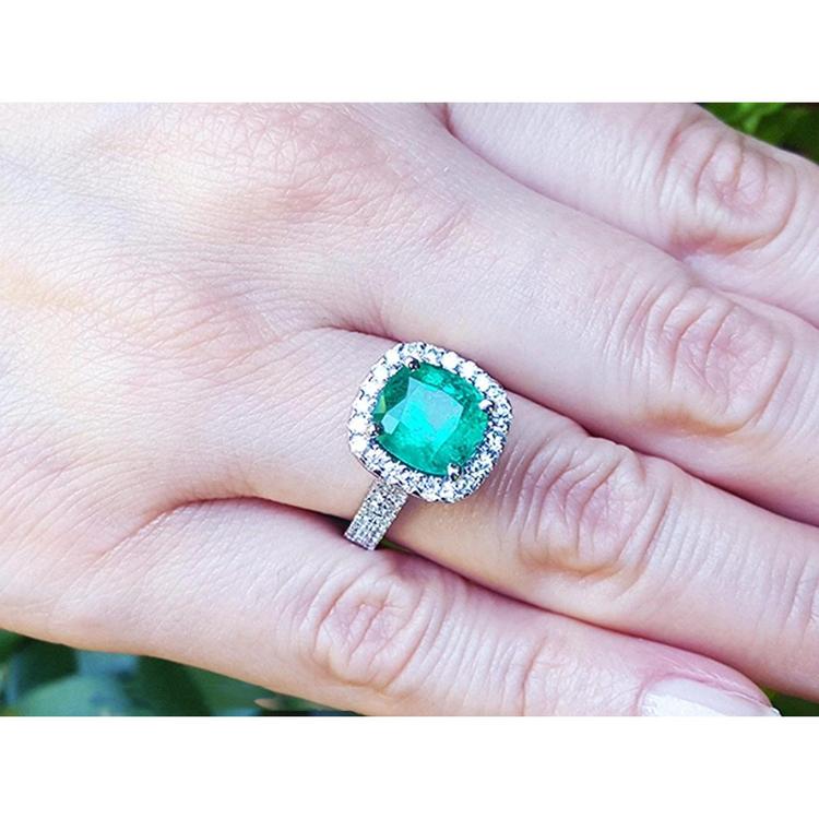 Cushion cut 3.92 ct natural emerald ring with diamond halo and band in 14K white gold on a hand.
