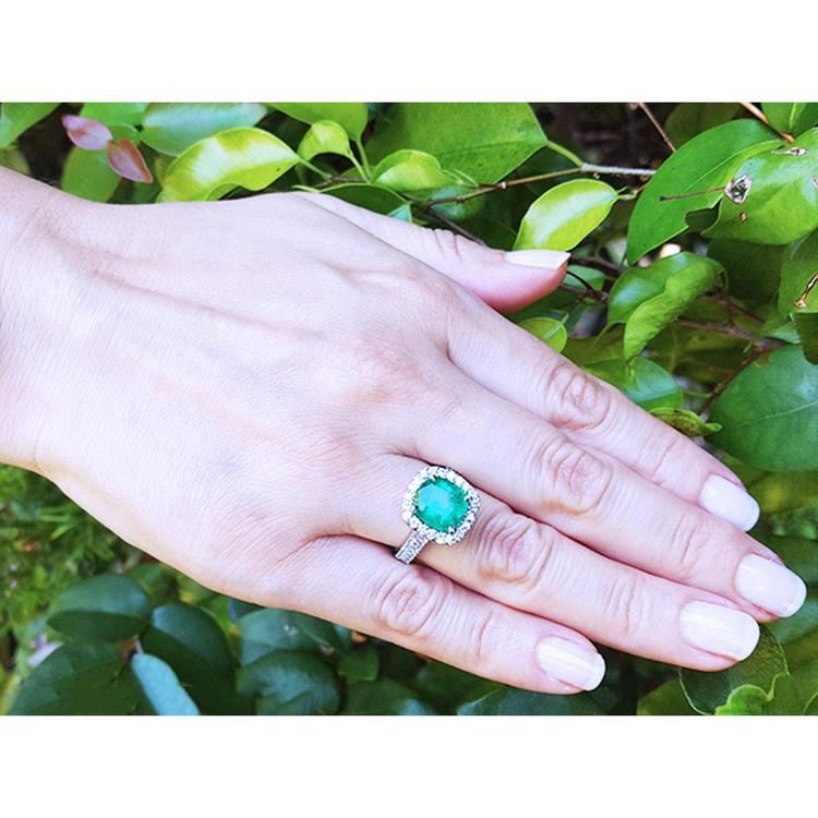 Cushion cut 3.92 ct. natural Colombian emerald ring with diamond halo in 14K white gold on a hand.