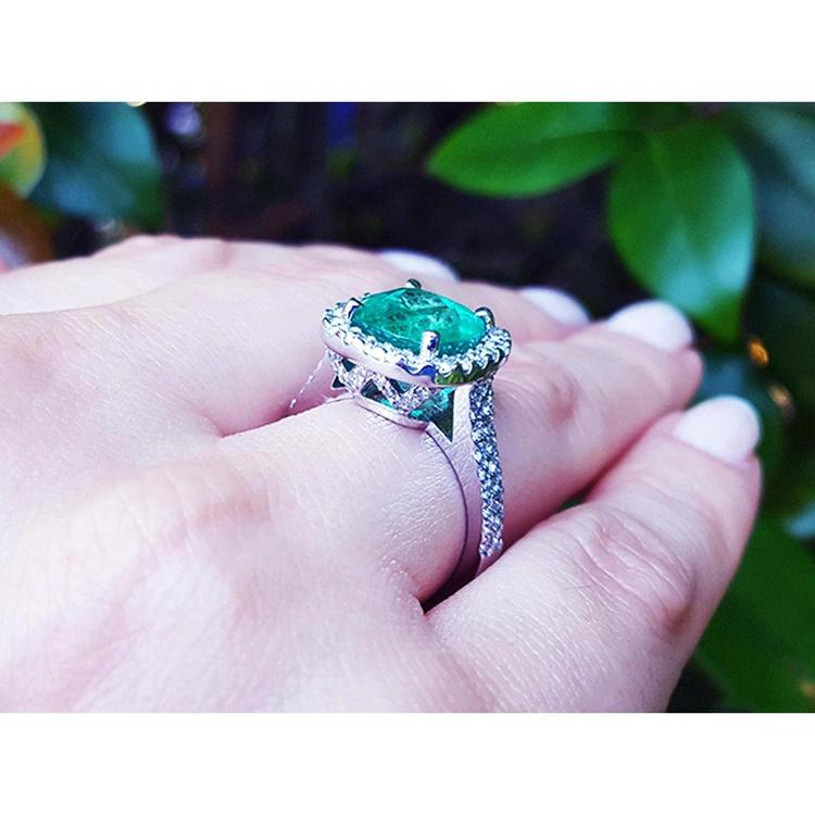 Cushion cut 3.92 ct. natural emerald ring with diamond halo on 14K white gold band, worn on a finger.