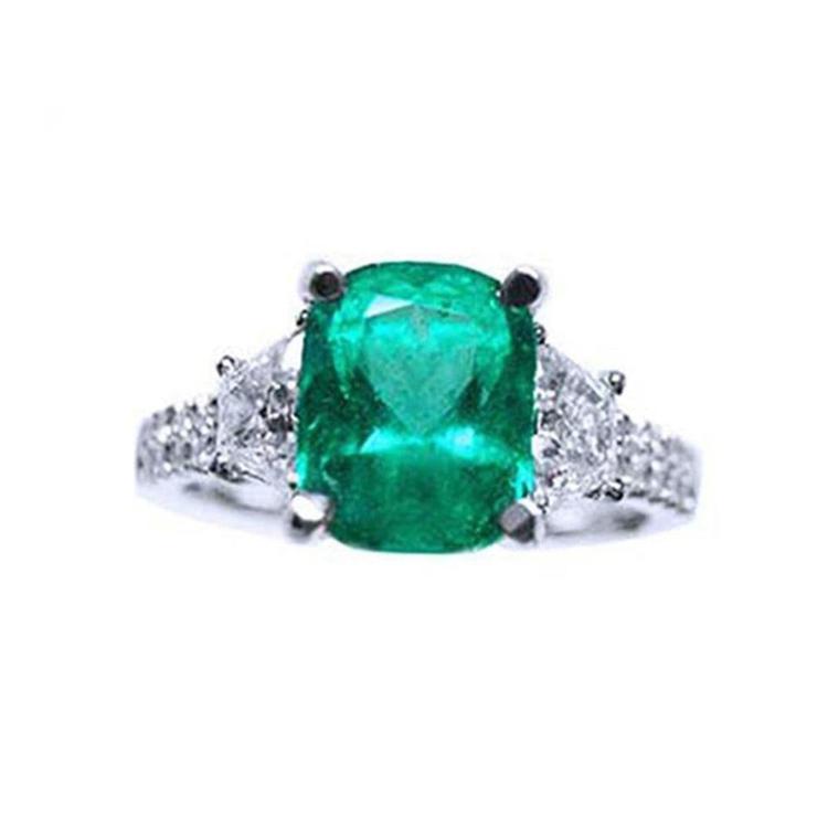 Ring with a cushion cut emerald gemstone and trapezoid diamond accents on each side in white gold.