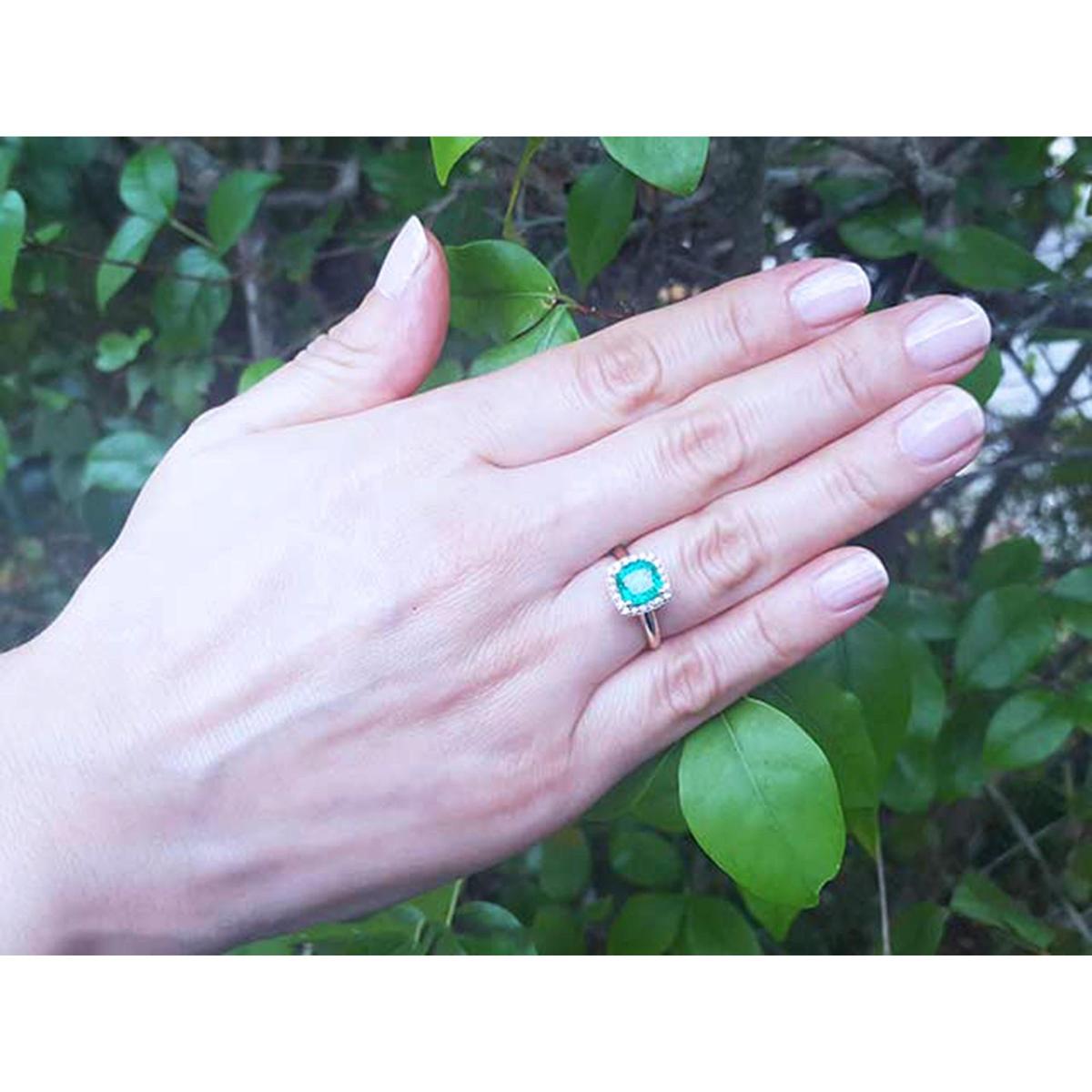 Hand wearing a cushion cut emerald ring with a leafy background.
