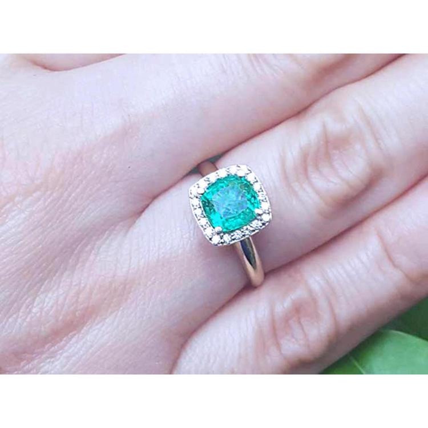 1.45 ct natural cushion-cut emerald halo diamond ring in 14K gold on a finger.