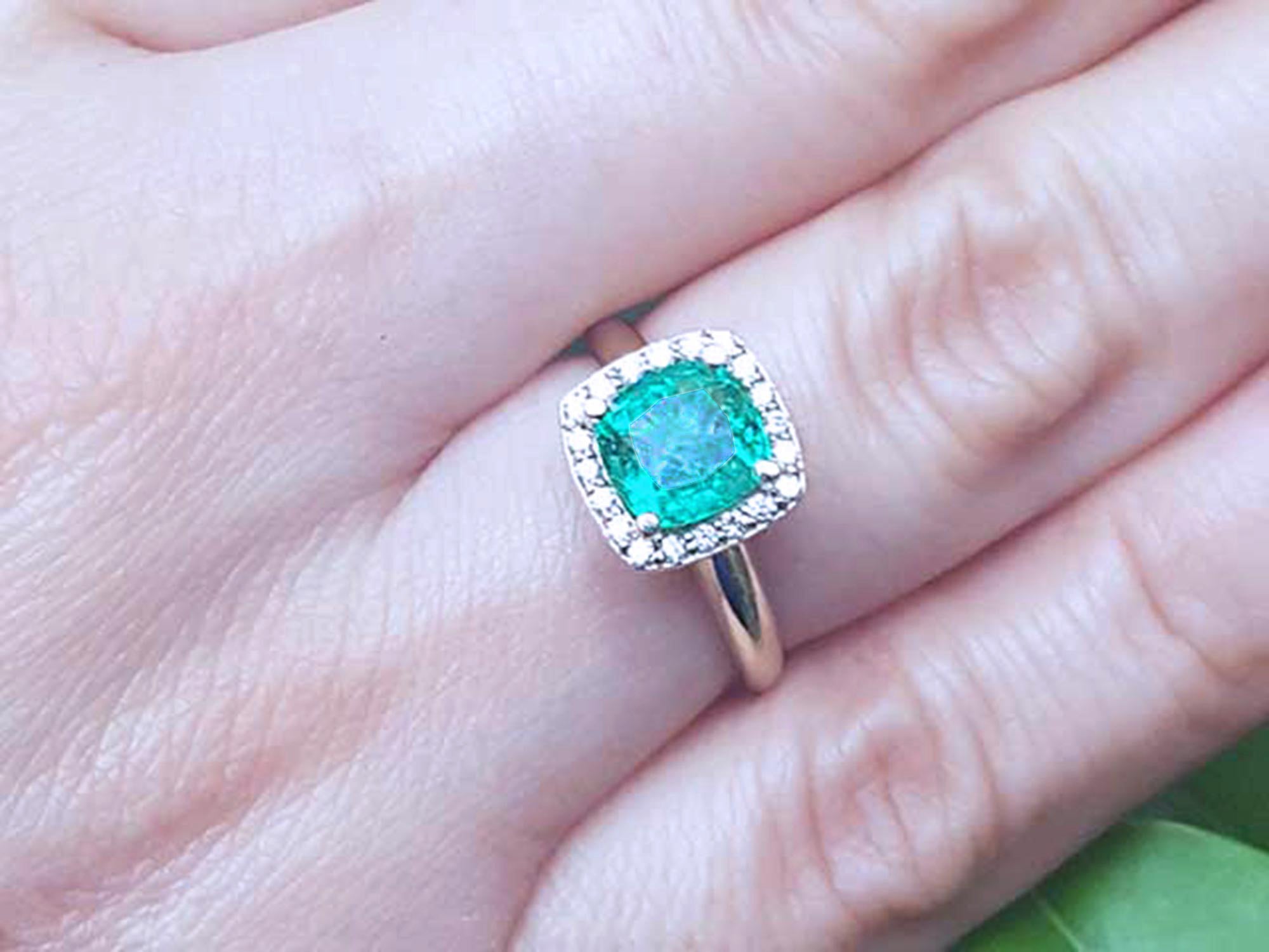 A women&#39;s cushion cut halo diamond emerald ring on a person&#39;s finger.