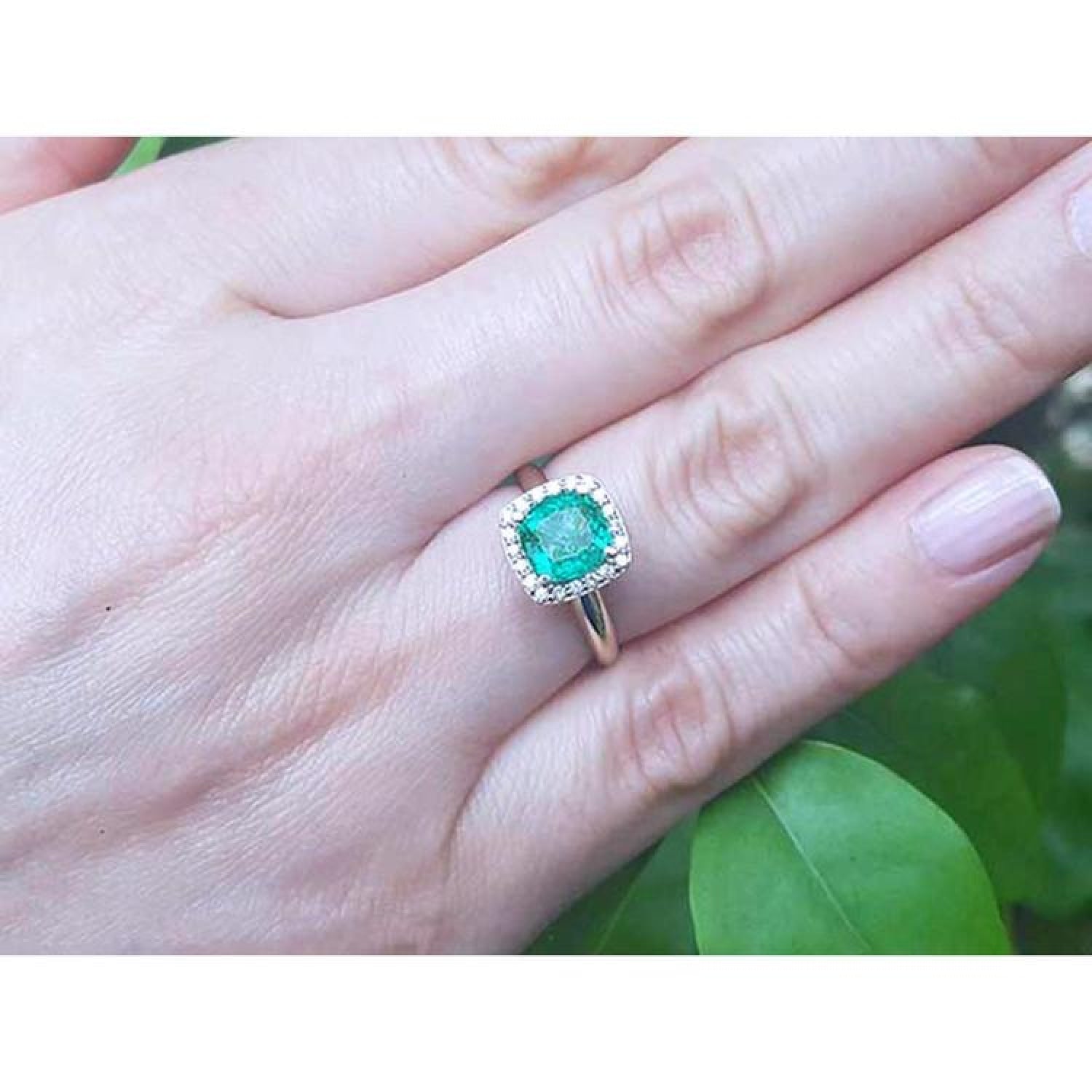 1.45 ct natural cushion-cut emerald ring with diamond halo on a woman's hand.