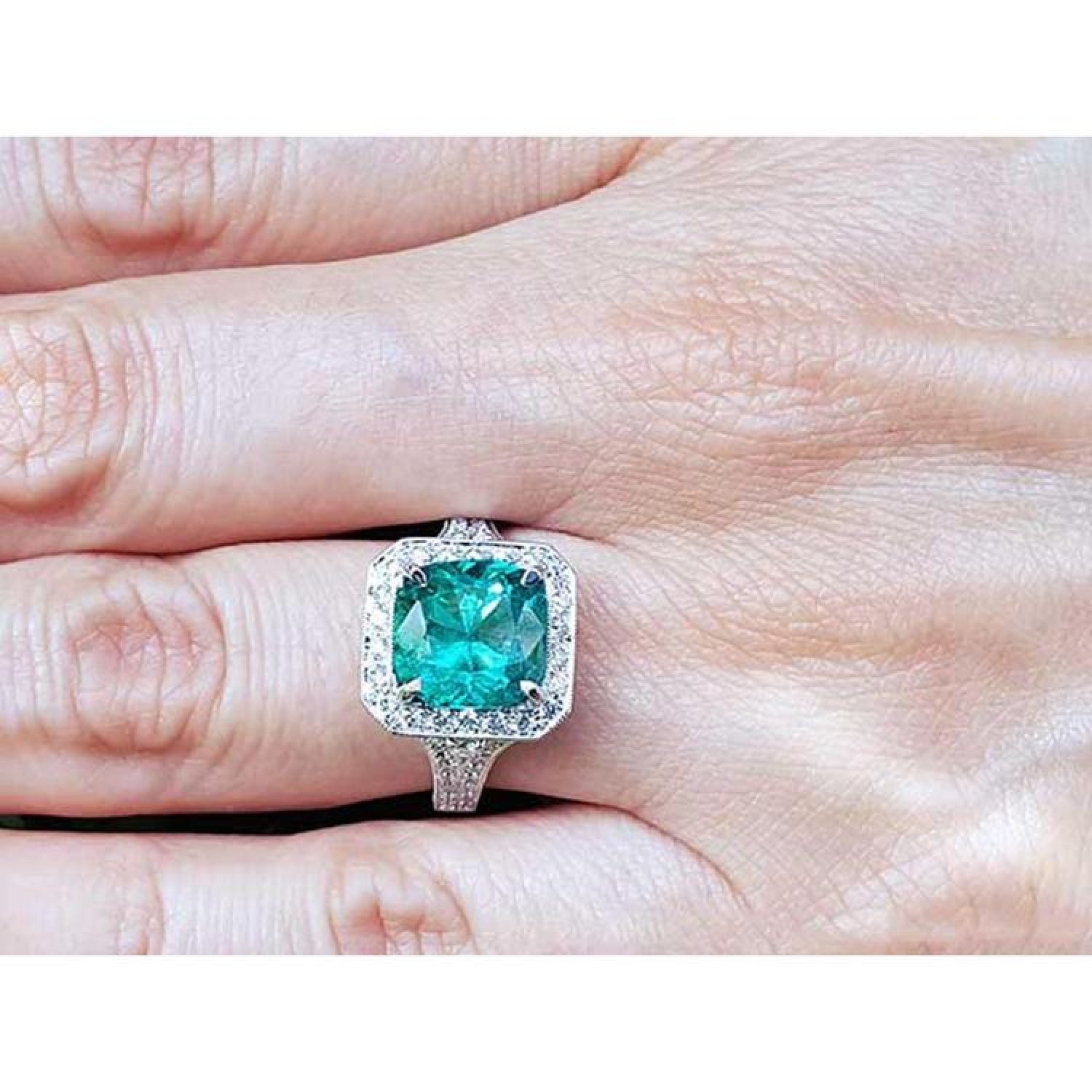 Cushion cut 3.68 ct Colombian emerald engagement ring with diamond halo in 18K white gold on a hand.