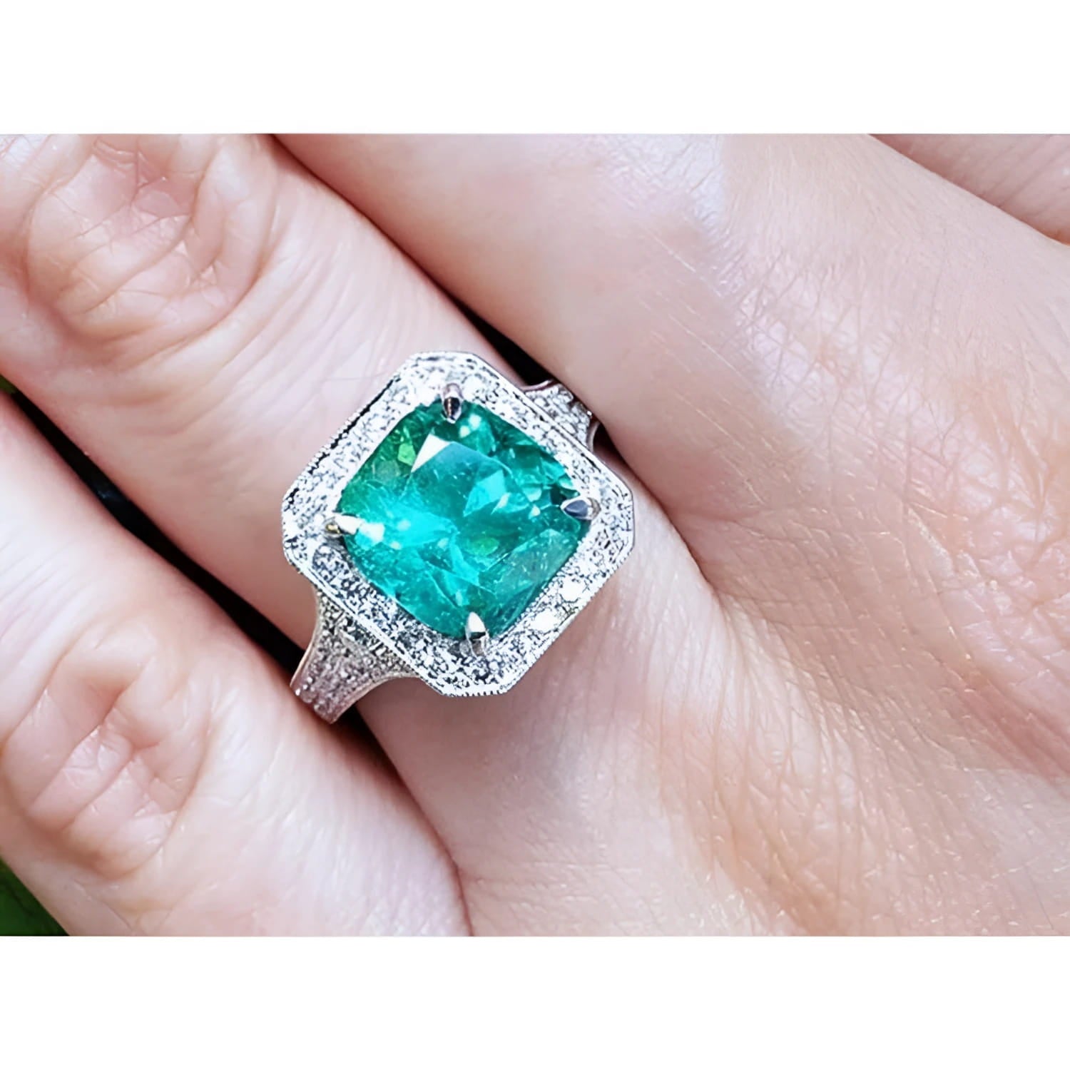 A lady's emerald ring cushion cut with a halo diamond crafted in 18k white gold on a finger.