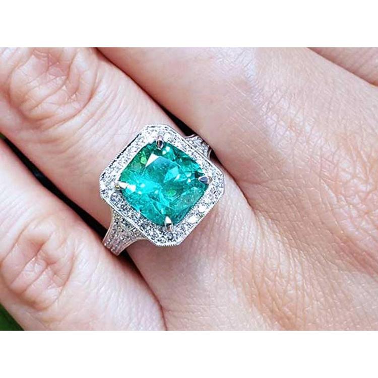A lady's emerald ring cushion cut with a halo diamond crafted in 18k white gold on a finger.
