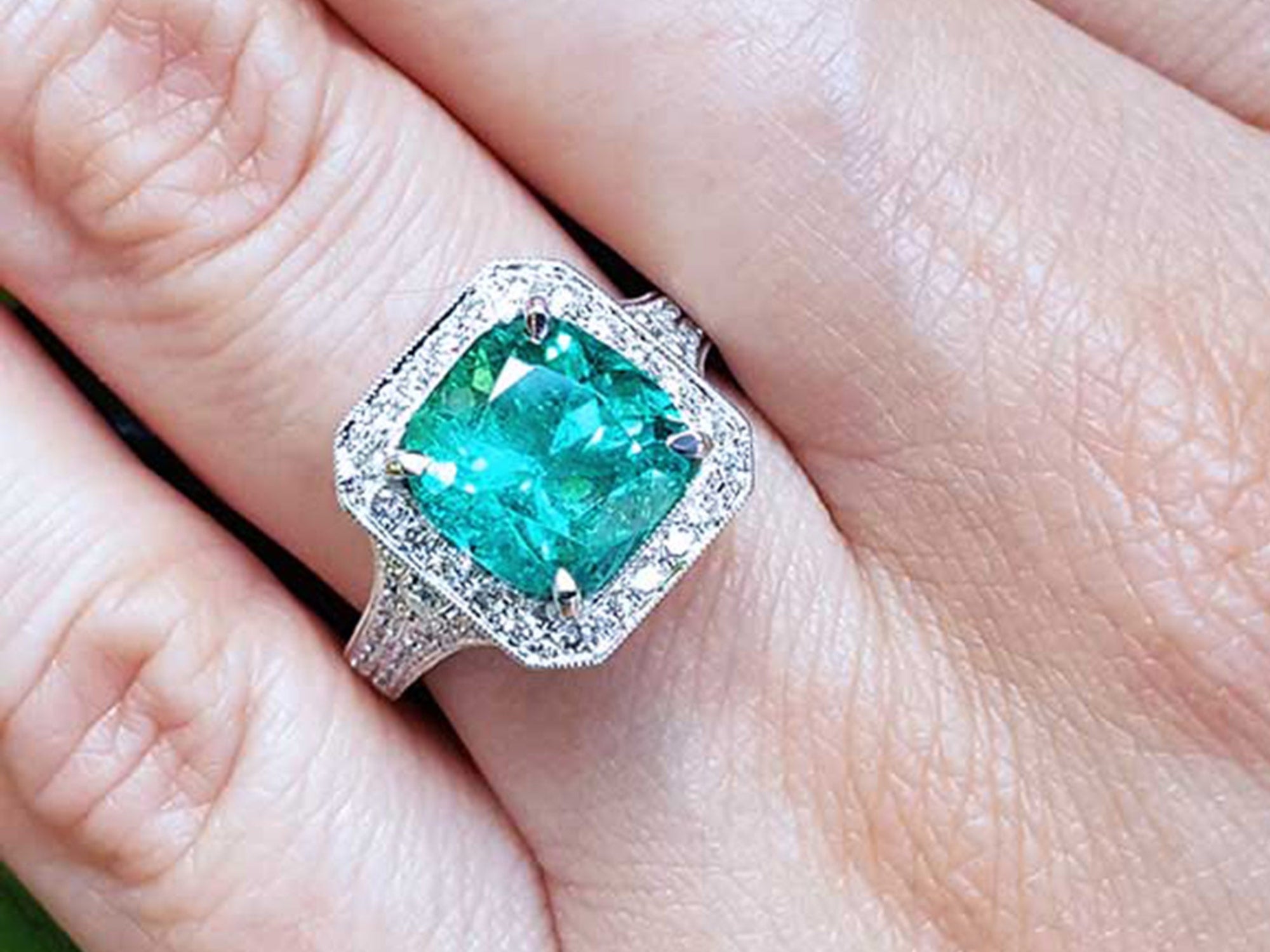 A lady's emerald ring cushion cut on a finger.