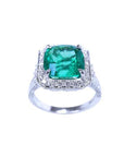 A cushion cut emerald white gold ring for women displaying a halo of natural diamond.