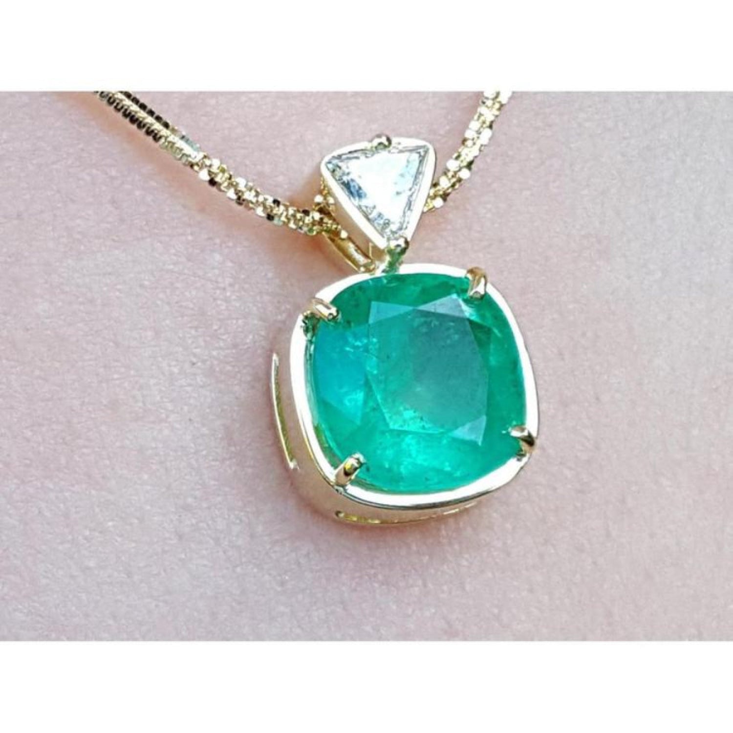 A genuine colombian emerald pendant with 18k yellow gold setting on a light skin background.