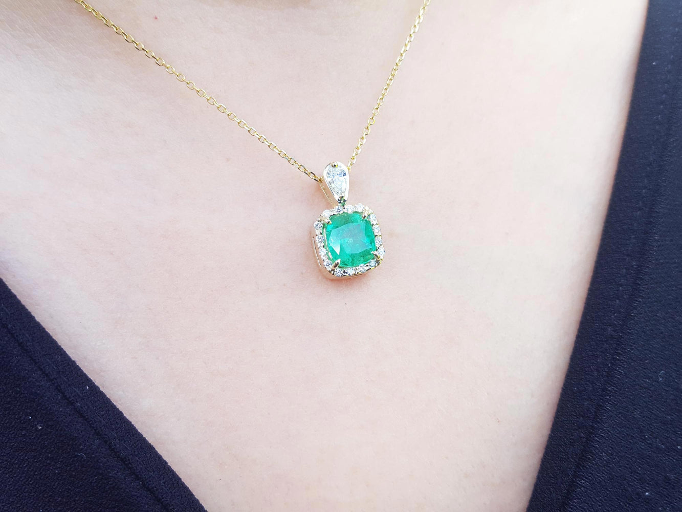 Gold necklace with a natural emerald pendant on a person wearing a black top.