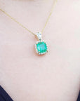 Gold necklace with a natural emerald pendant on a person wearing a black top.
