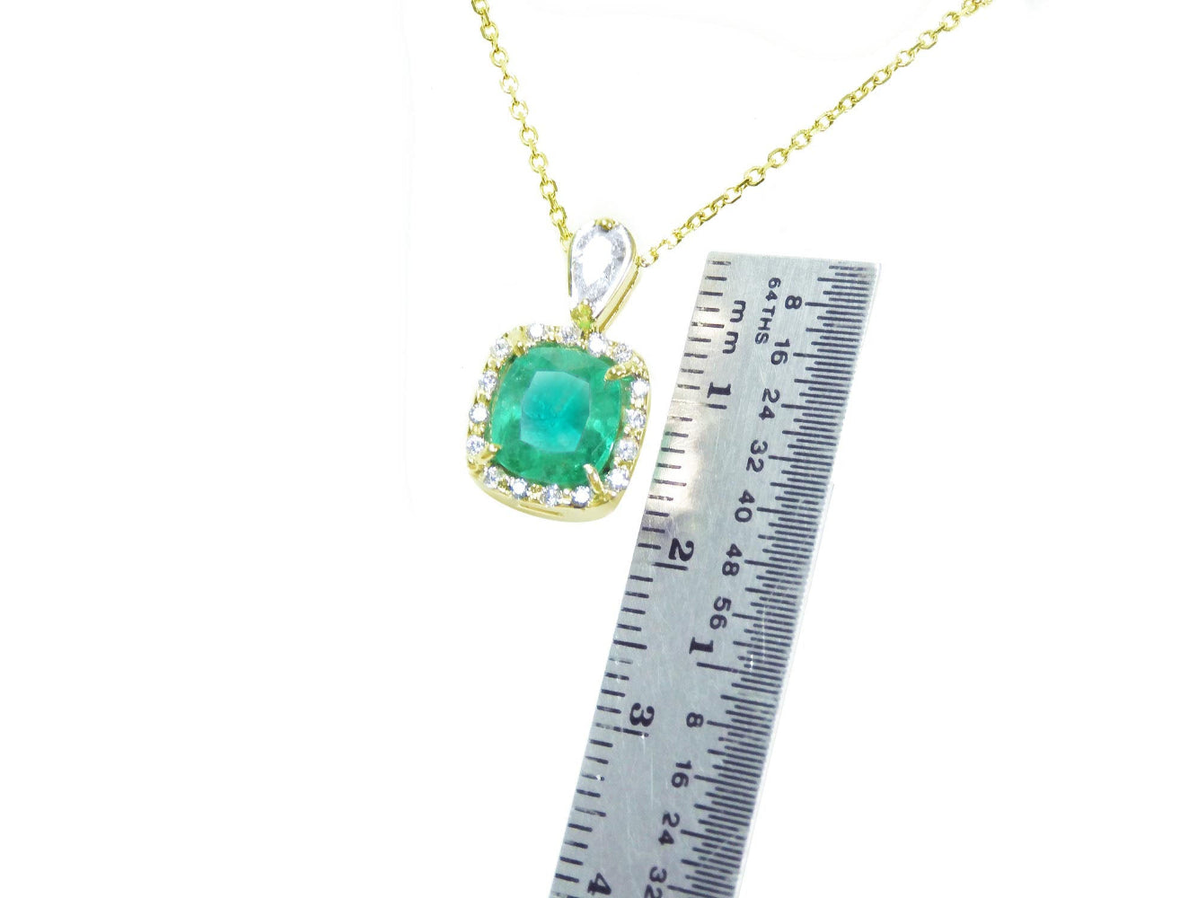 Gold necklace with a cushion natural emerald pendant next to a ruler for size reference on a white background