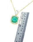 Gold necklace with a cushion natural emerald pendant next to a ruler for size reference on a white background