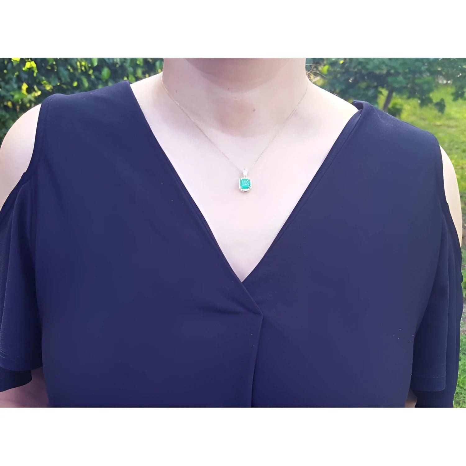 Cushion-cut emerald pendant with halo natural diamonds on a 14K yellow gold chain, worn on a model.