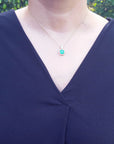 Navy blue dress with a cushion cut emerald pendant necklace on a woman's neck against a green outdoor background.