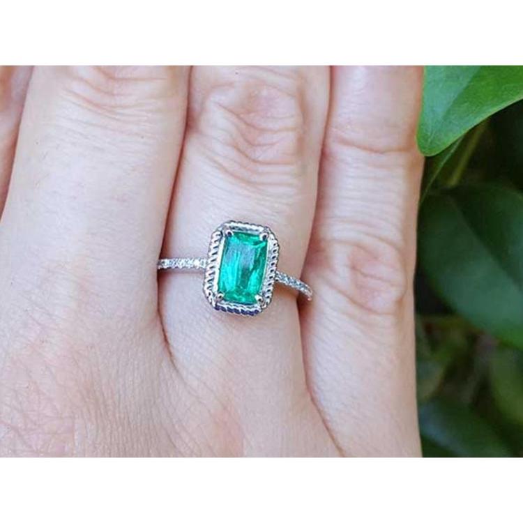 A cushion cut natural colombian emerald ring made of 14k white gold on a finger.