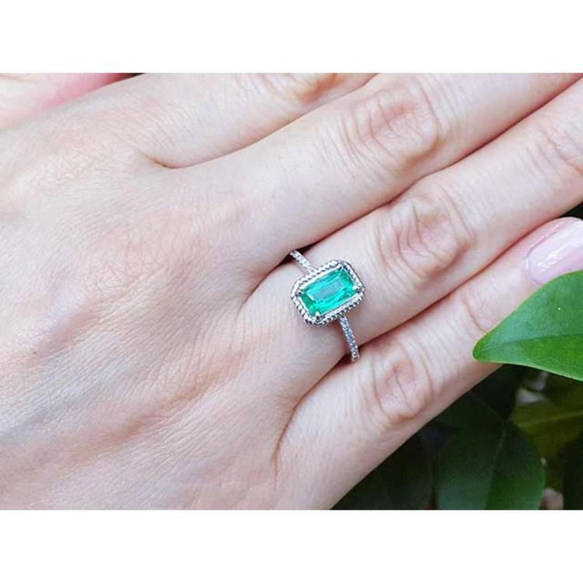 14K white gold cushion-cut emerald solitaire ring with rope detailing on a hand.