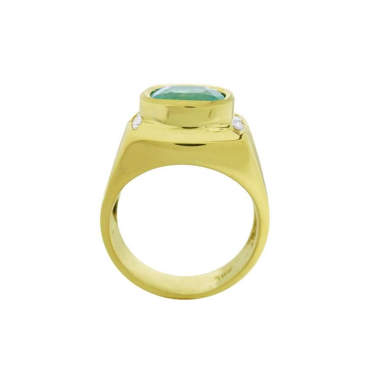 Men's gold ring with a natural emerald on a lateral position, top setting and band design displayed.