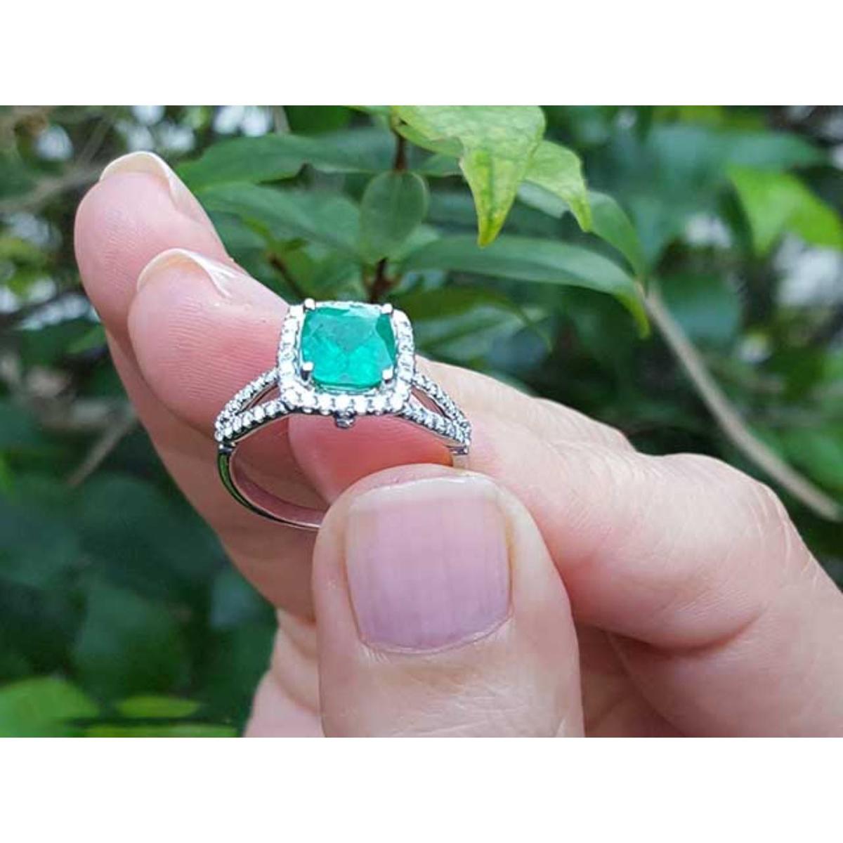 Held between fingers a bridal's emerald engagement ring with a green leafy background.