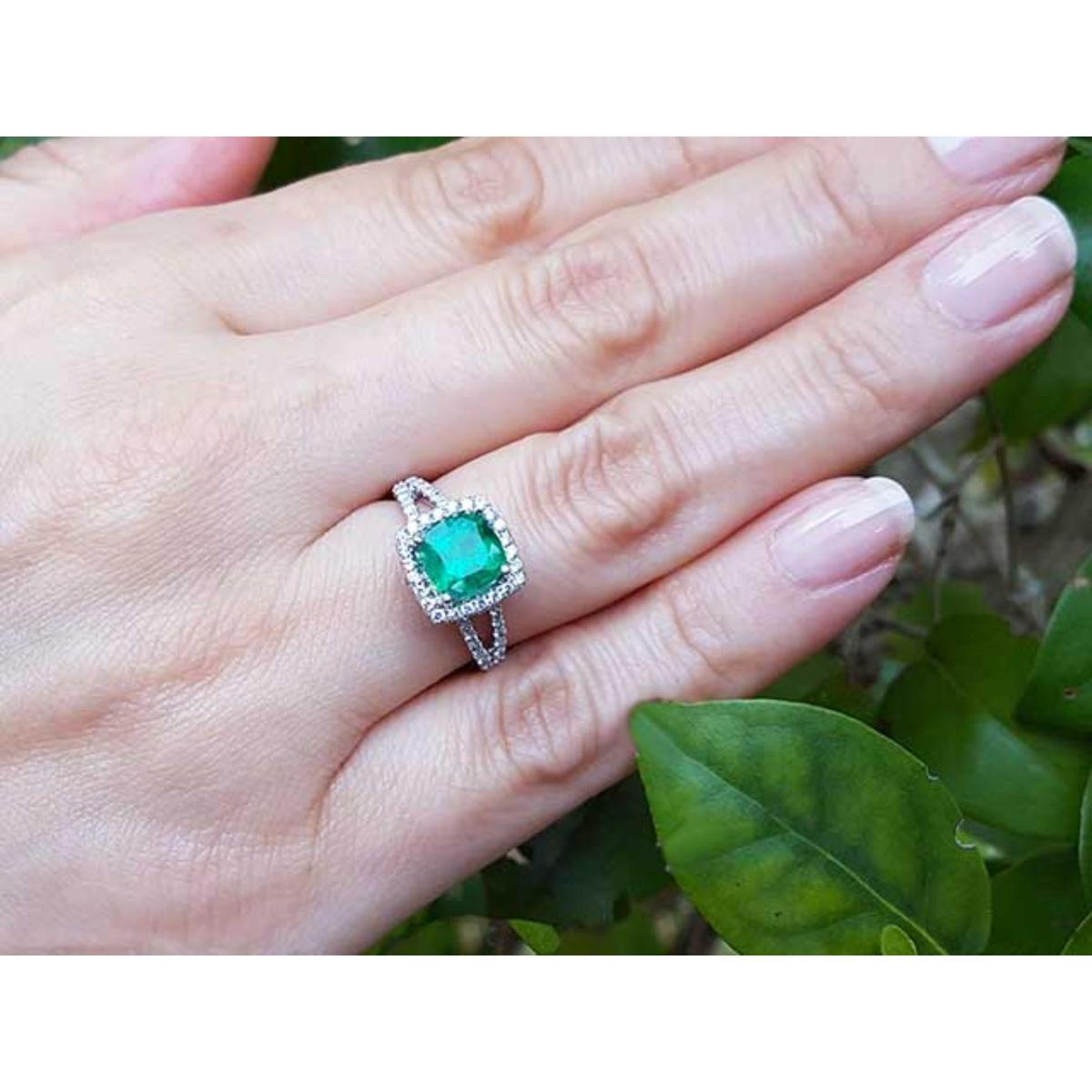 Hand wearing a cushion cut colombian emerald ring against a natural background.