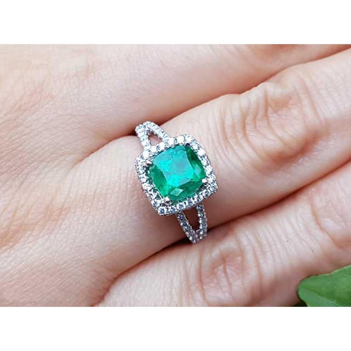 A natural emerald cushion cut in a halo diamond with sides split shank on a finger.