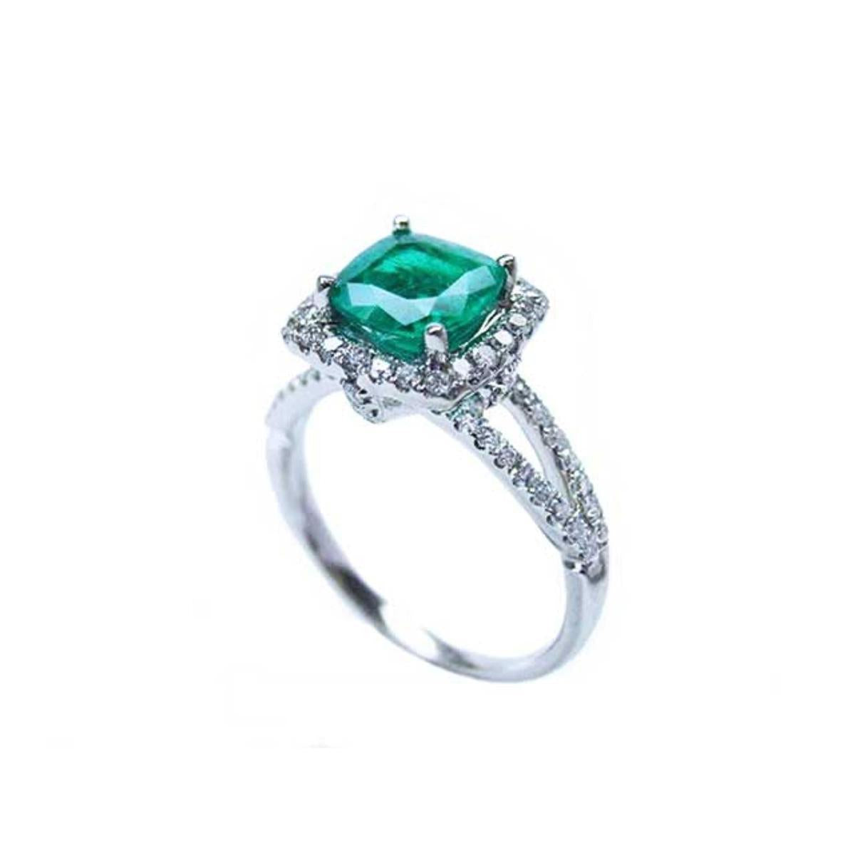 A colombian emerald cushion cut on top of the white gold ring with diamond accents, side split shank profile view.