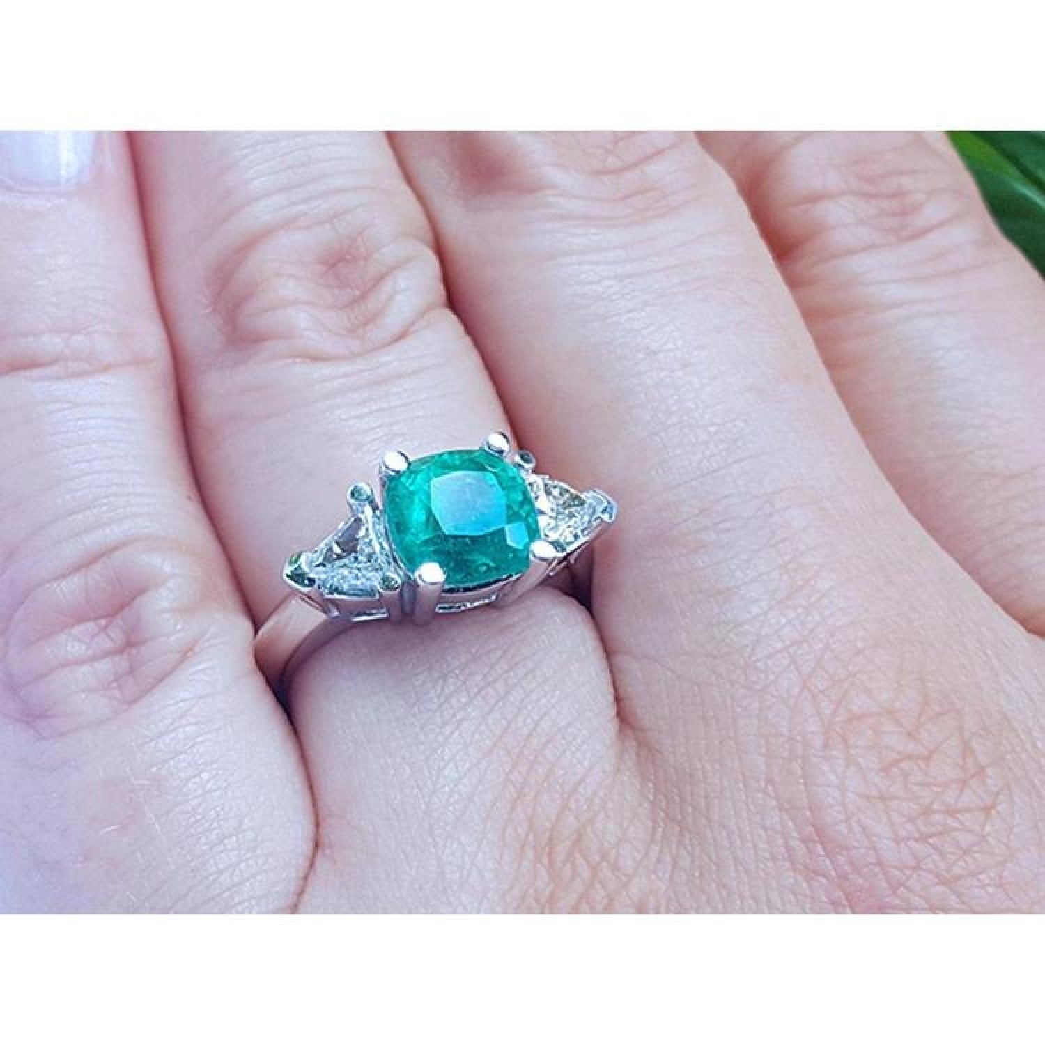 2.18 ct cushion cut emerald ring with trillion side diamonds in 14K white gold on a hand.
