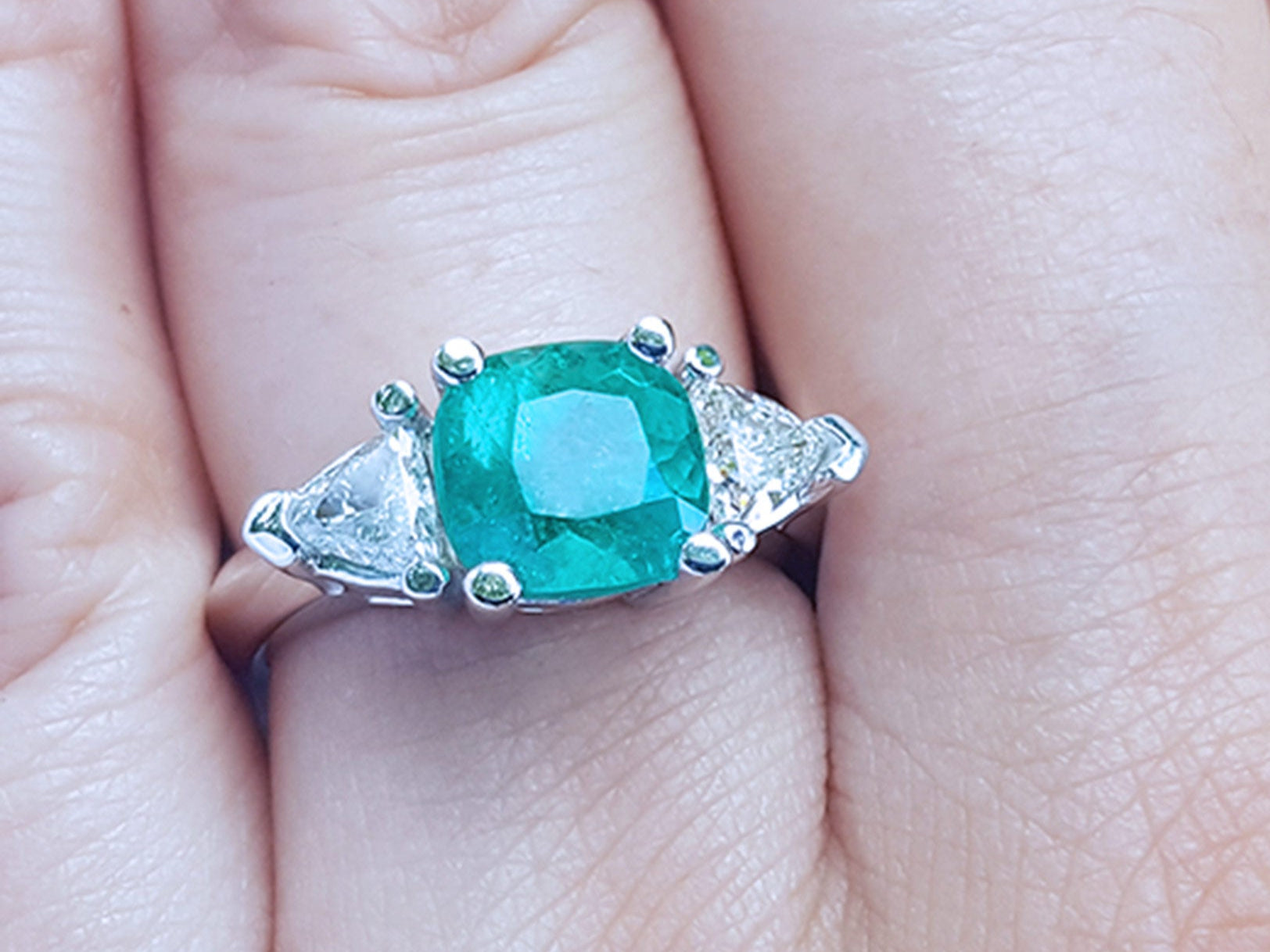 Emerald ring with trillion side diamond accents on a finger.