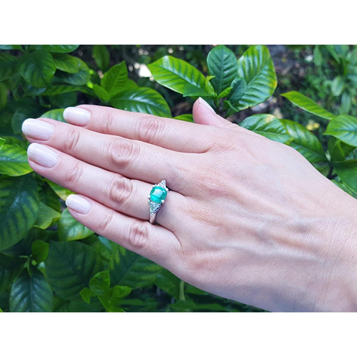 Hand wearing a genuine emerald and trillion side diamond rings for women with a leafy background.