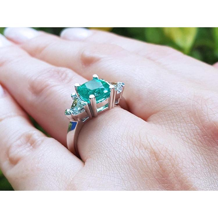 2.18 ct cushion cut emerald ring with trillion side diamonds on a hand, 14K white gold.