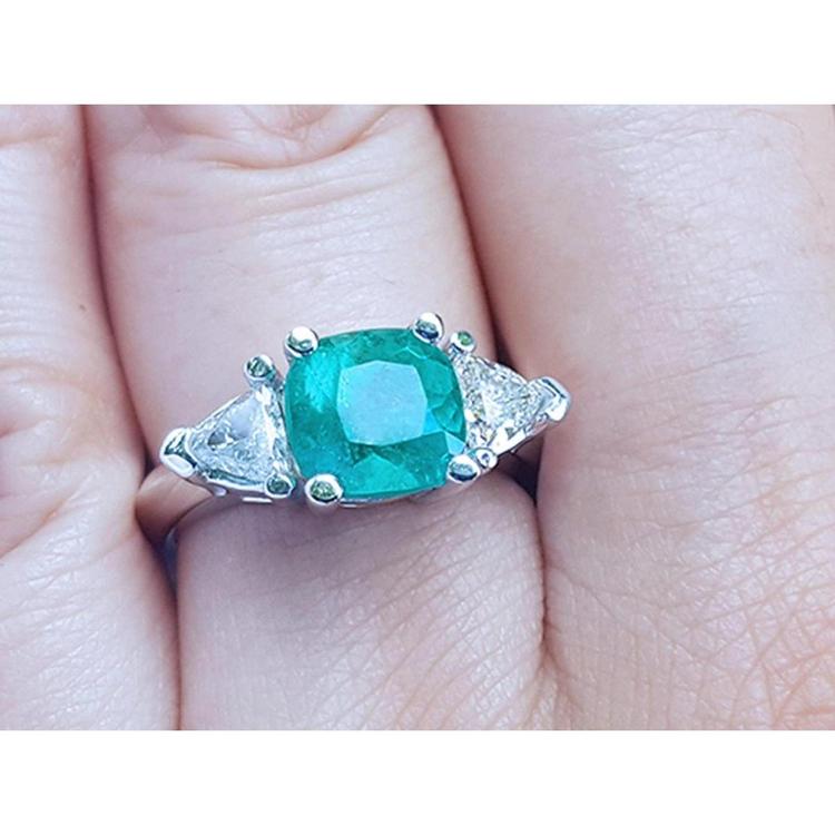 Emerald ring with trillion side diamond accents made in 14k white gold on a finger.