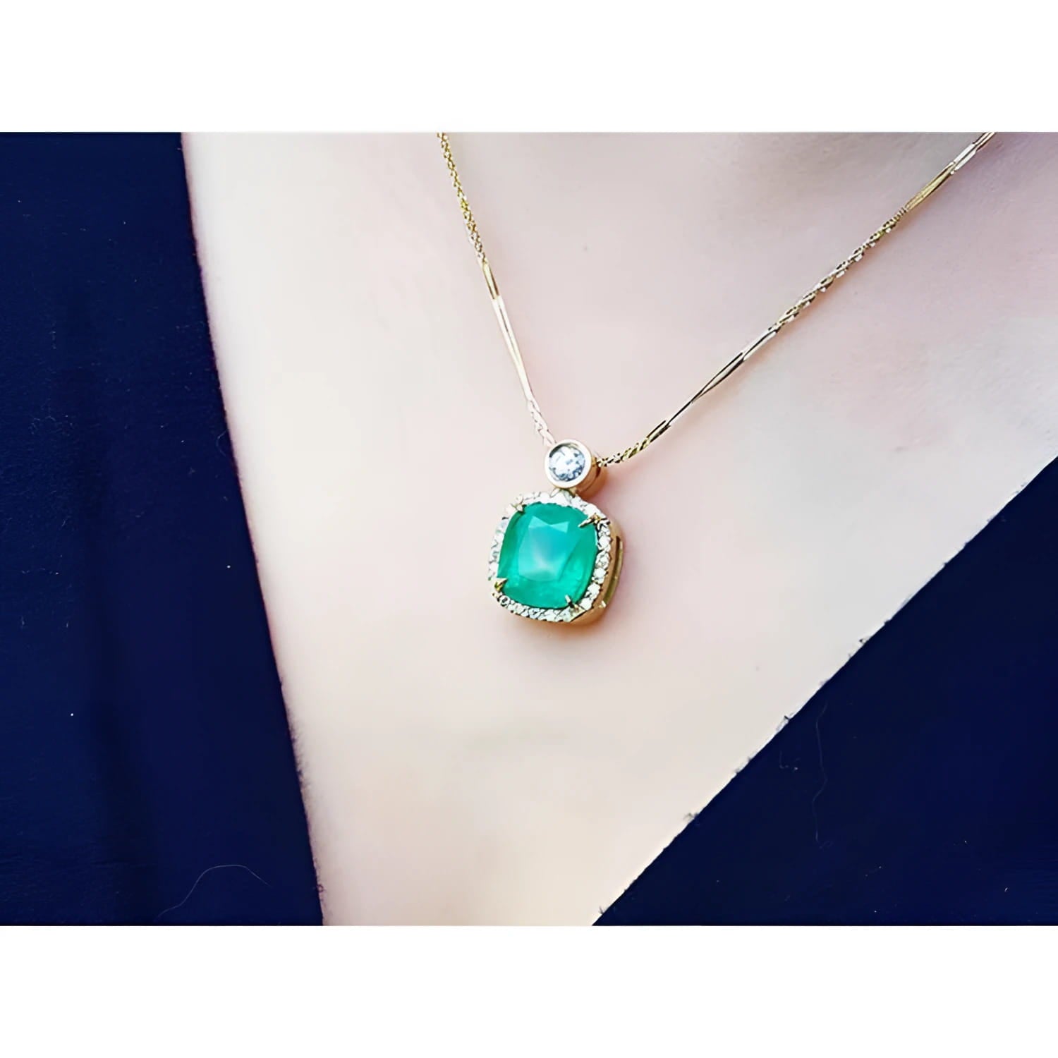 Cushion cut emerald necklace in 18K yellow gold with diamond halo and solitaire, worn on a person.