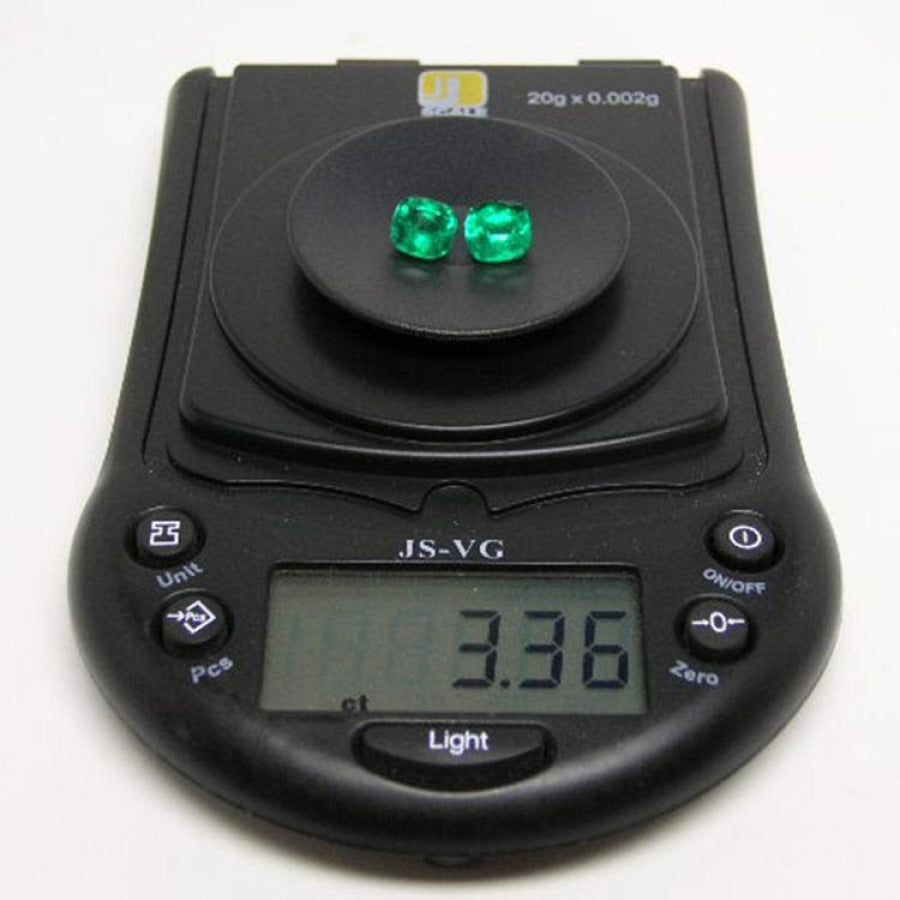 Matched pair of 3.36 carat cushion cut green emeralds on a black digital scale.