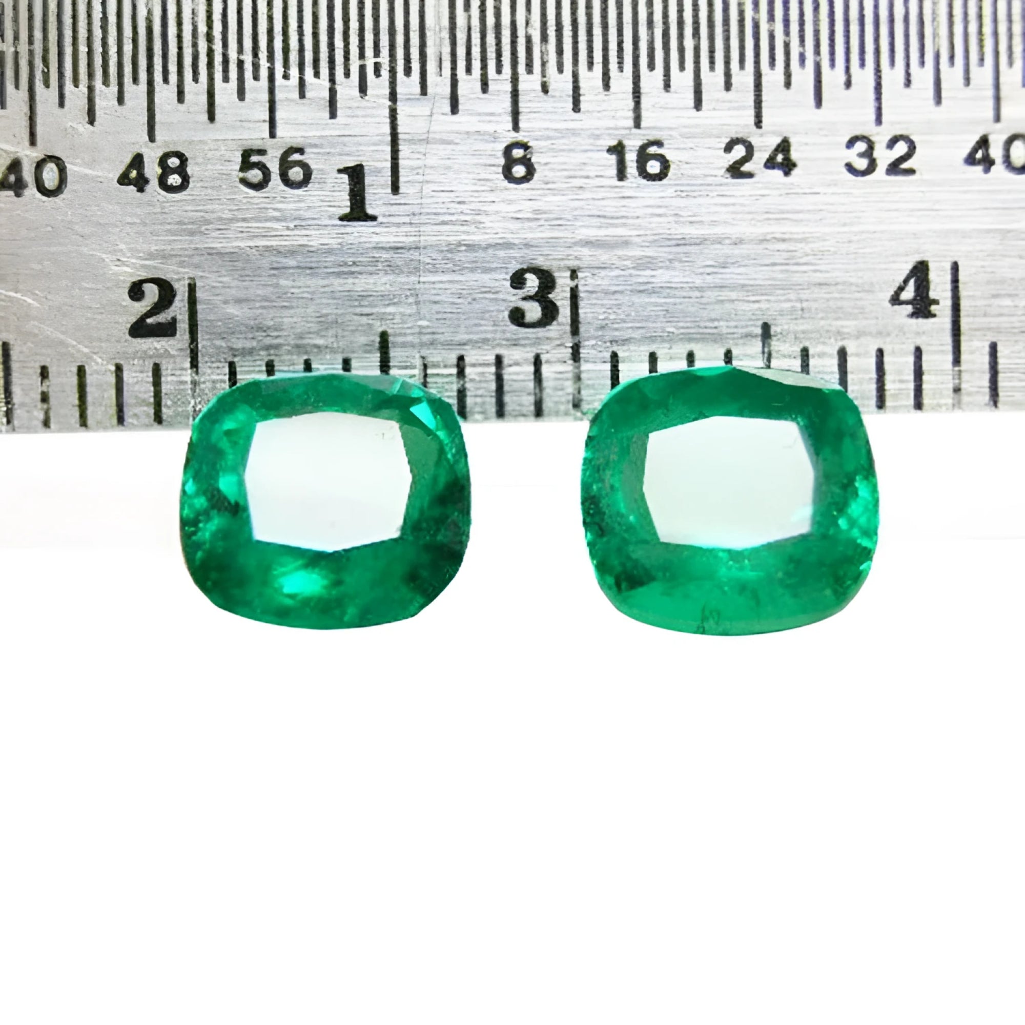 Matched pair of vibrant green cushion cut emeralds, 3.36 carats total, displayed with a ruler for scale.