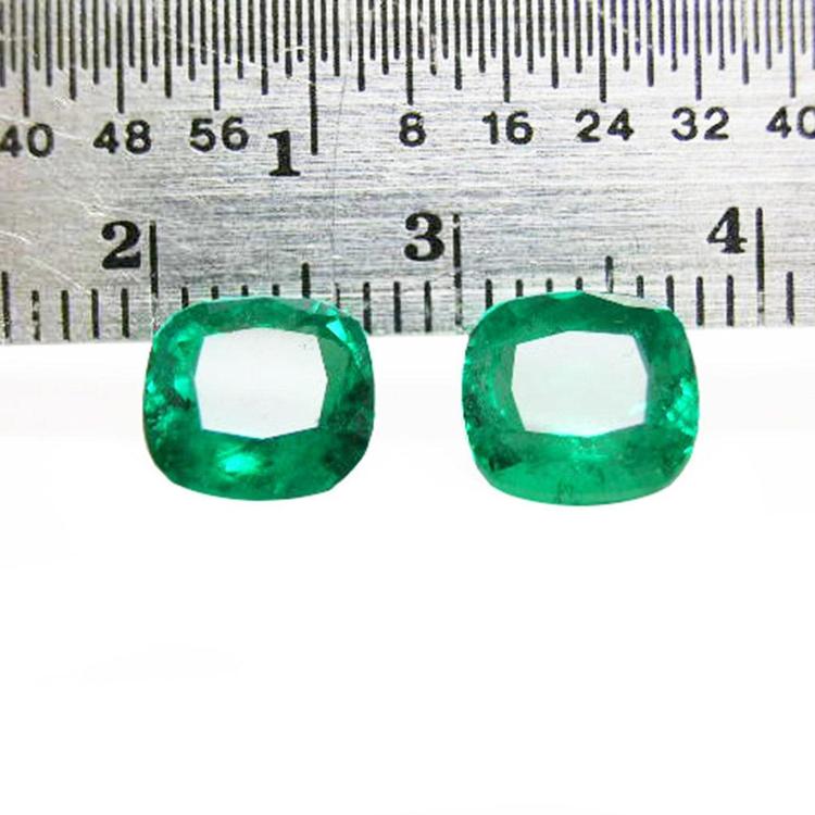 Matched pair of vibrant green cushion cut emeralds, 3.36 carats total, displayed with a ruler for scale.