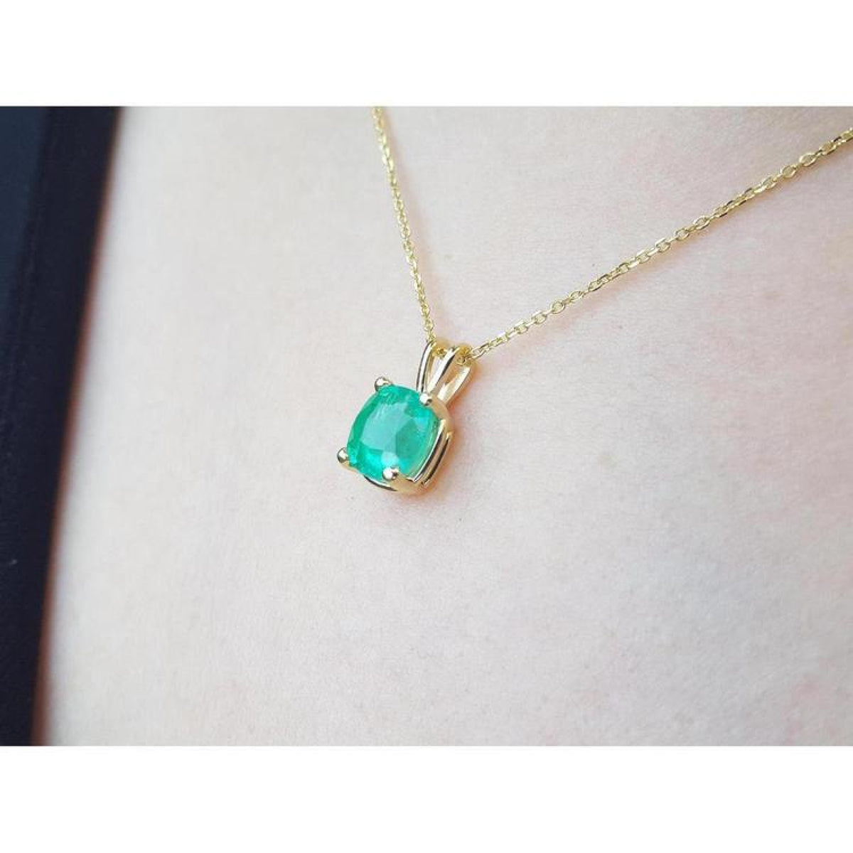 Cushion cut natural emerald solitaire pendant in 14K yellow gold, worn on a neck.