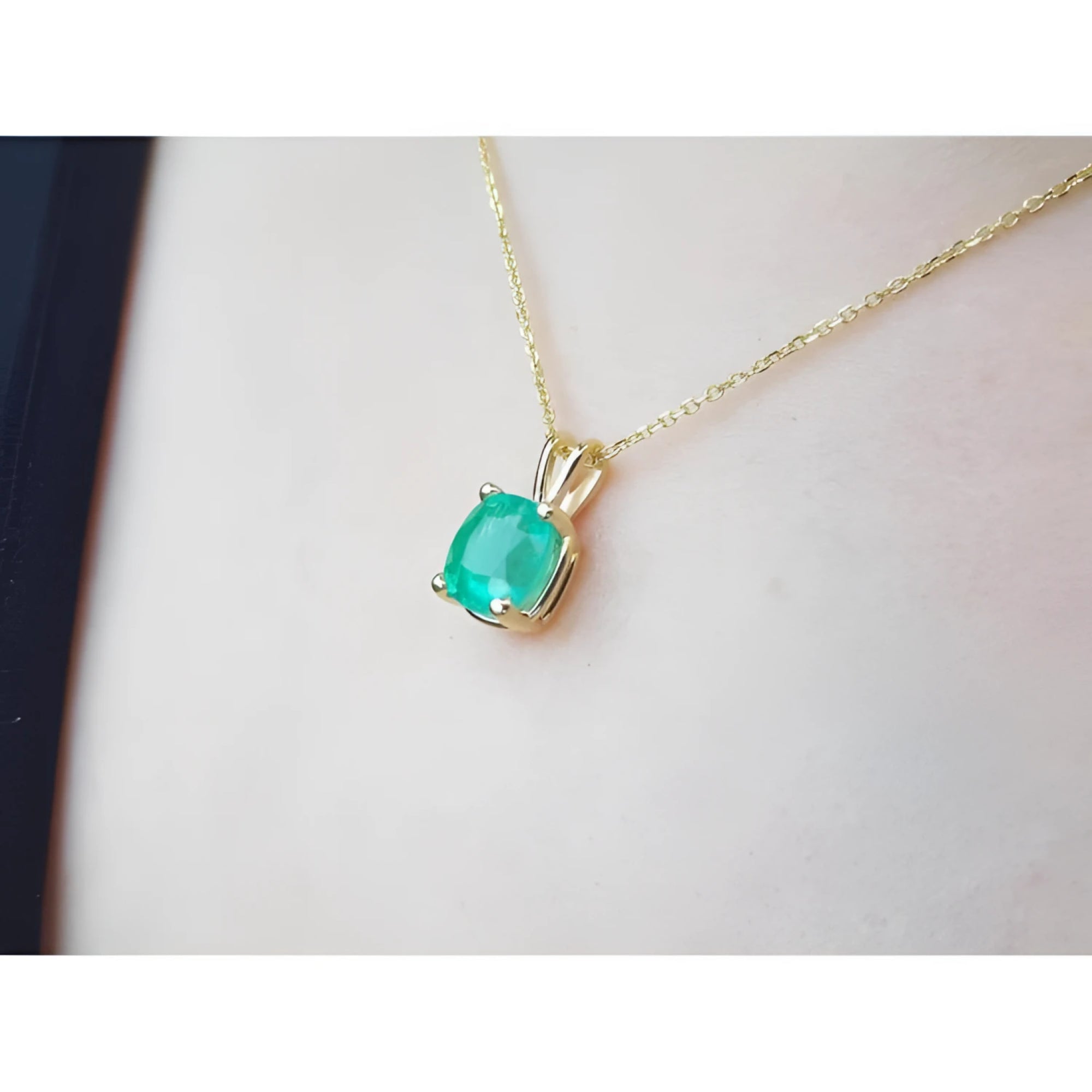 Cushion cut natural emerald solitaire pendant in 14K yellow gold, worn on a neck.