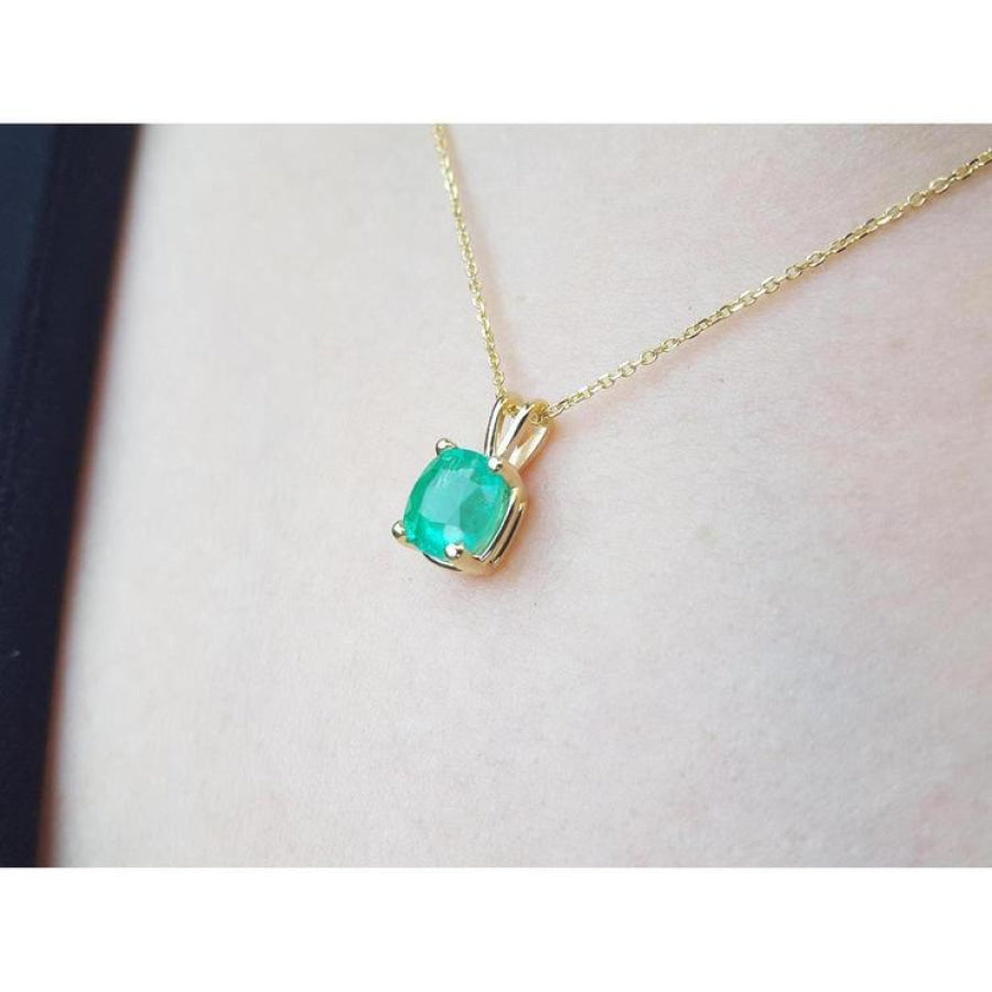 Cushion cut natural emerald solitaire pendant in 14K yellow gold, worn on a neck.