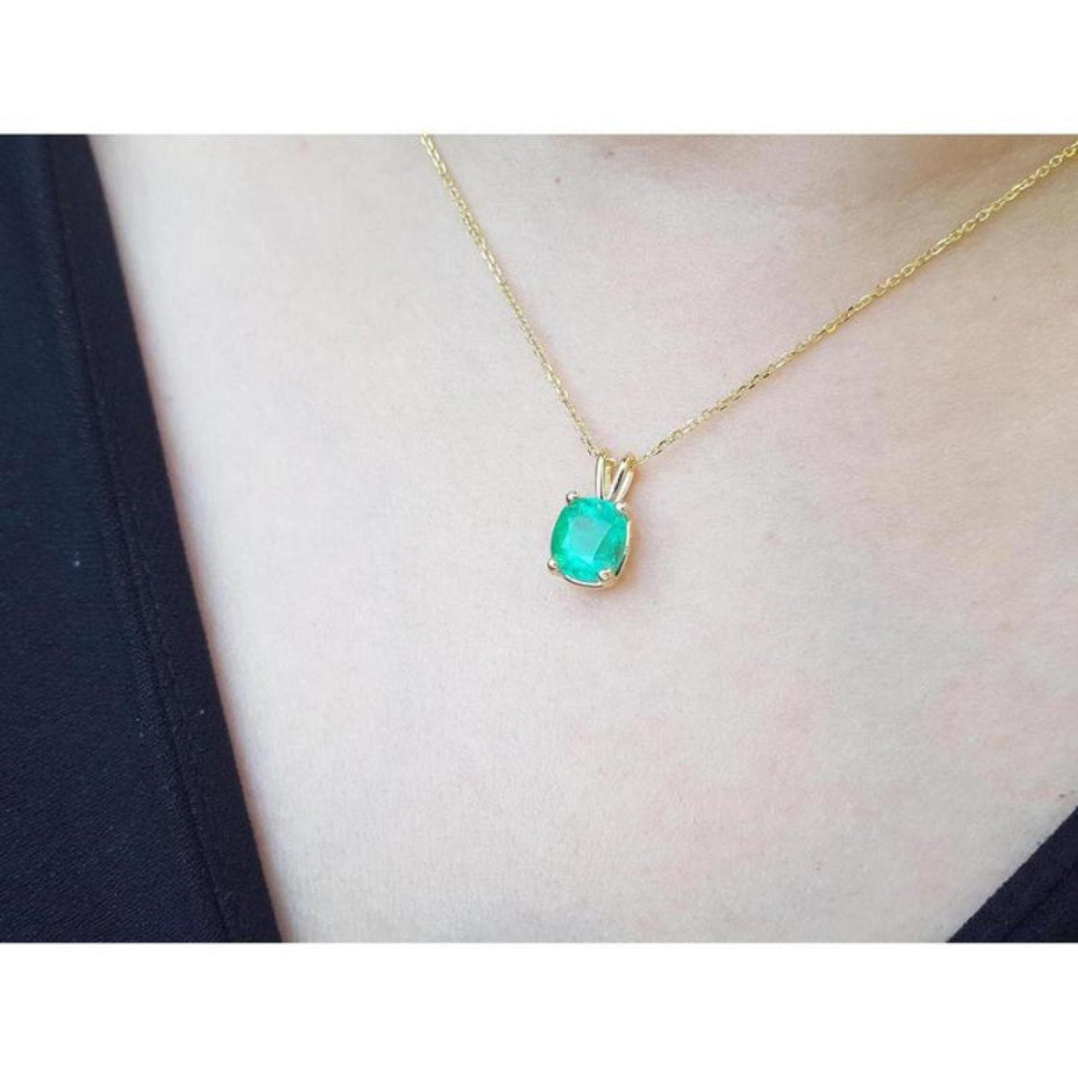 Cushion cut natural emerald solitaire pendant in 14K yellow gold, worn on a neck.