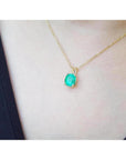 Cushion cut natural emerald solitaire pendant in 14K yellow gold, worn on a neck.