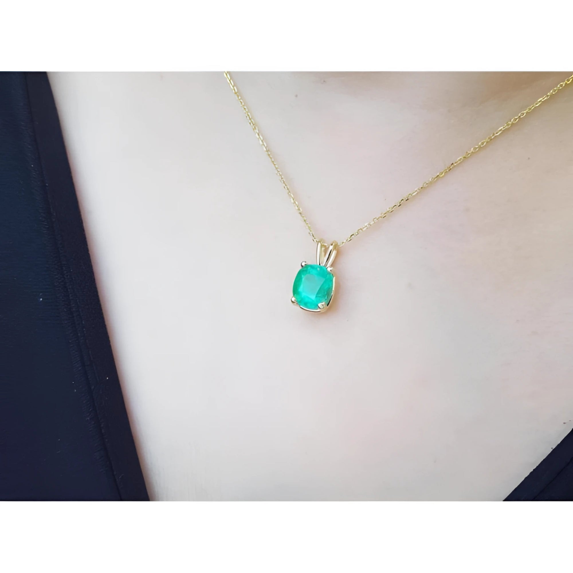 Cushion cut natural emerald solitaire pendant in 14K yellow gold, worn on a neck.