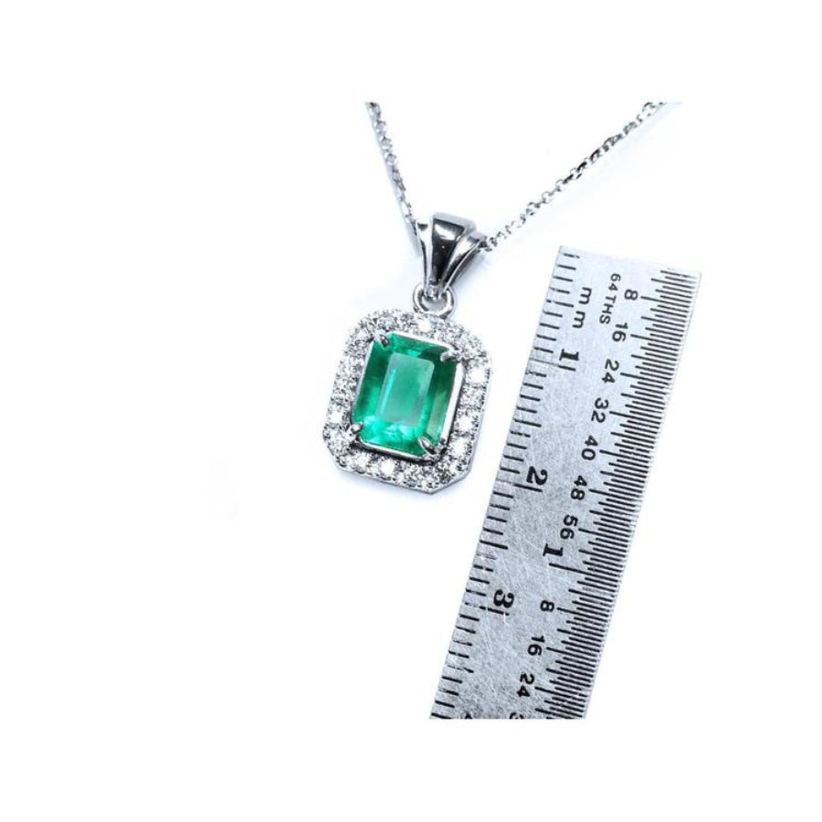 Emerald-cut Colombian emerald pendant with halo diamonds in 14K white gold, shown with a ruler for scale.