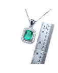 Emerald-cut Colombian emerald pendant with halo diamonds in 14K white gold, shown with a ruler for scale.