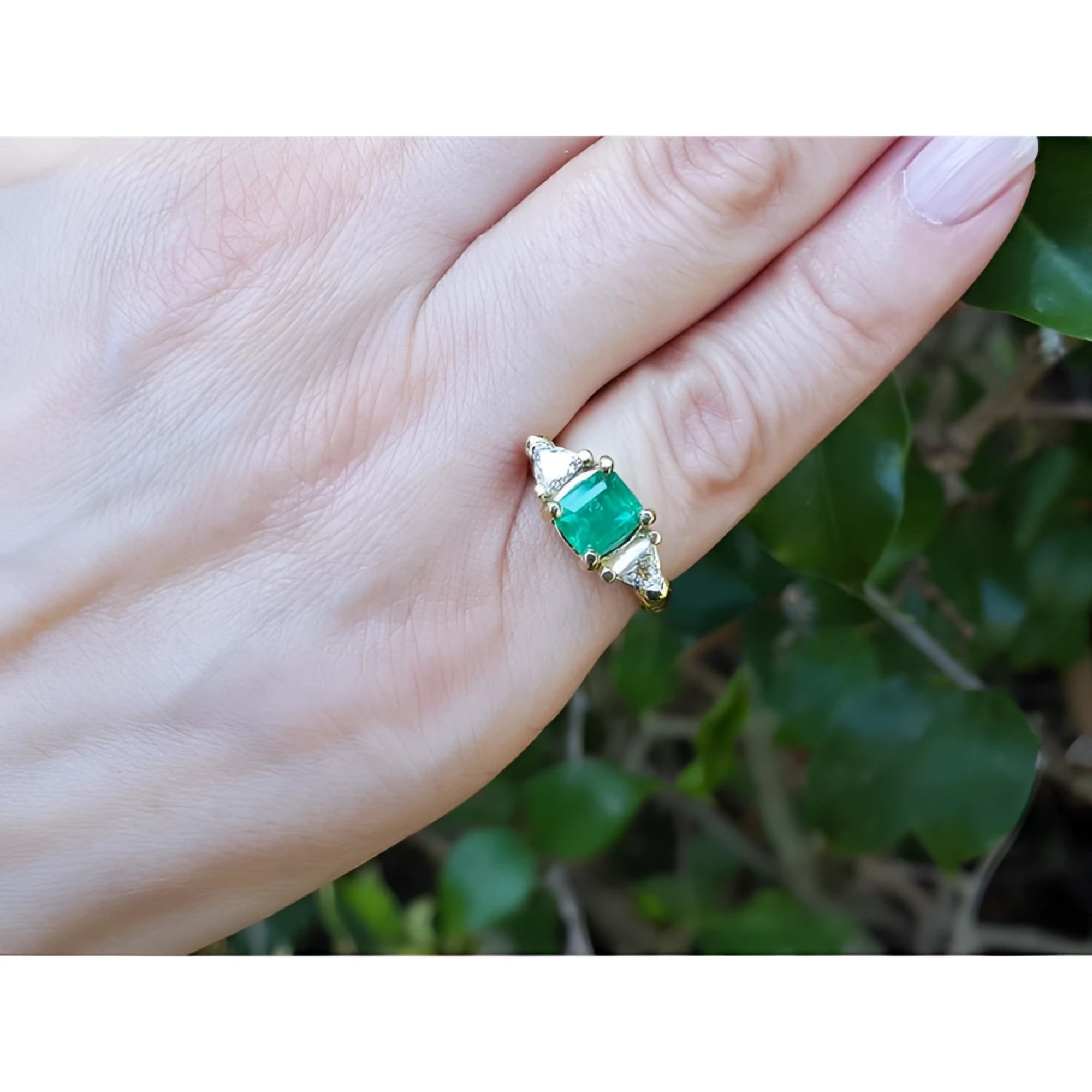 1.47 ct. emerald-cut Colombian emerald ring with trillion diamonds in 18k yellow gold on a hand.